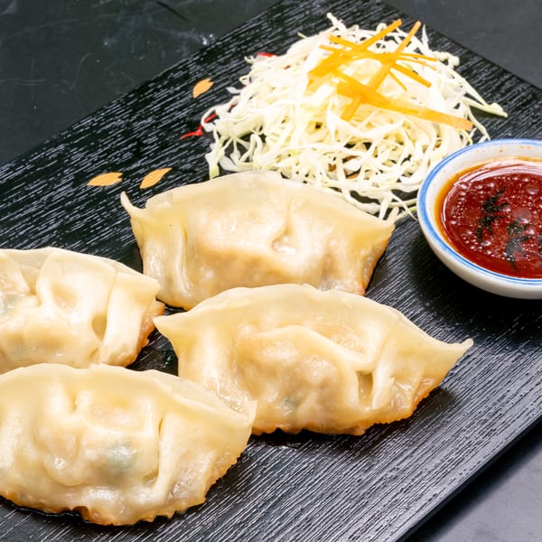Four golden-brown dumplings, shredded cabbage, and a small bowl of dipping sauce on a black plate.