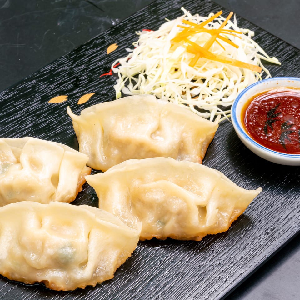 Four golden-brown dumplings, shredded cabbage, and a small bowl of dipping sauce on a black plate.