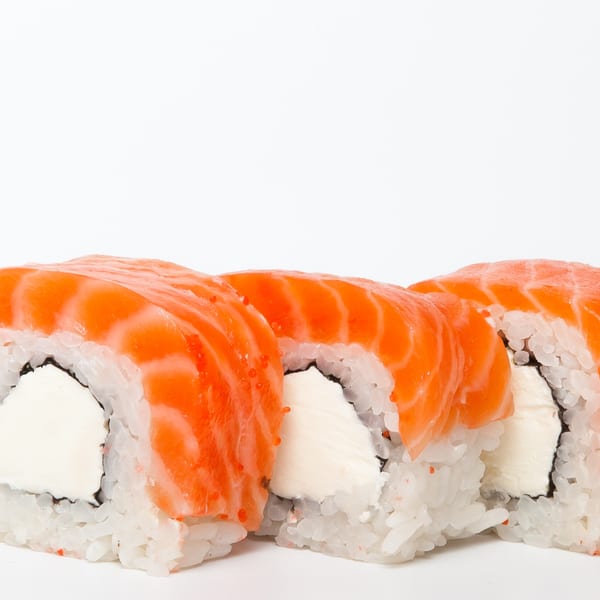 Three salmon sushi rolls with cream cheese filling and rice, on a white background.