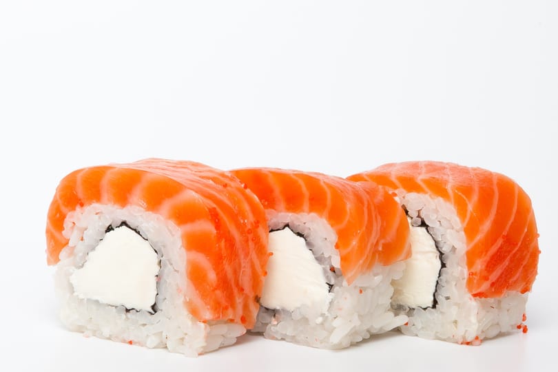 Three salmon sushi rolls with cream cheese filling and rice, on a white background.