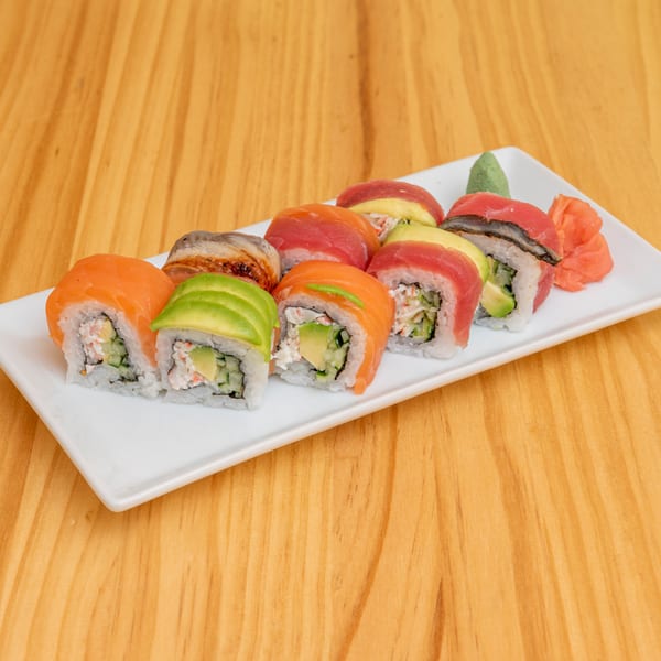 A white rectangular plate holds ten colorful sushi rolls, with ginger and wasabi on a wooden table.