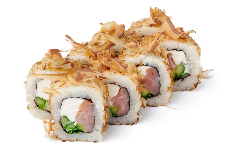Four sushi rolls with salmon, cream cheese, and cucumber, topped with bonito flakes.